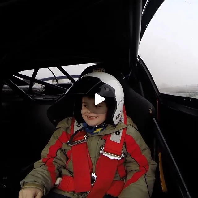 Niño sonriendo con casco a bordo de un coche de competición